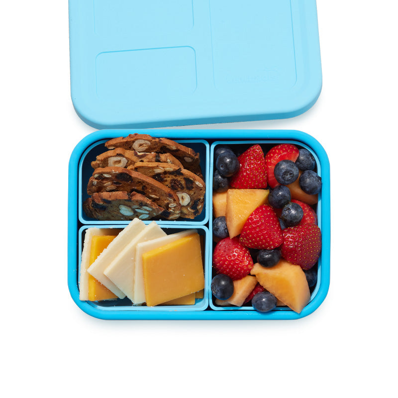 A blue bento box with interchangeable compartments containing various food items such as fruits and nuts.